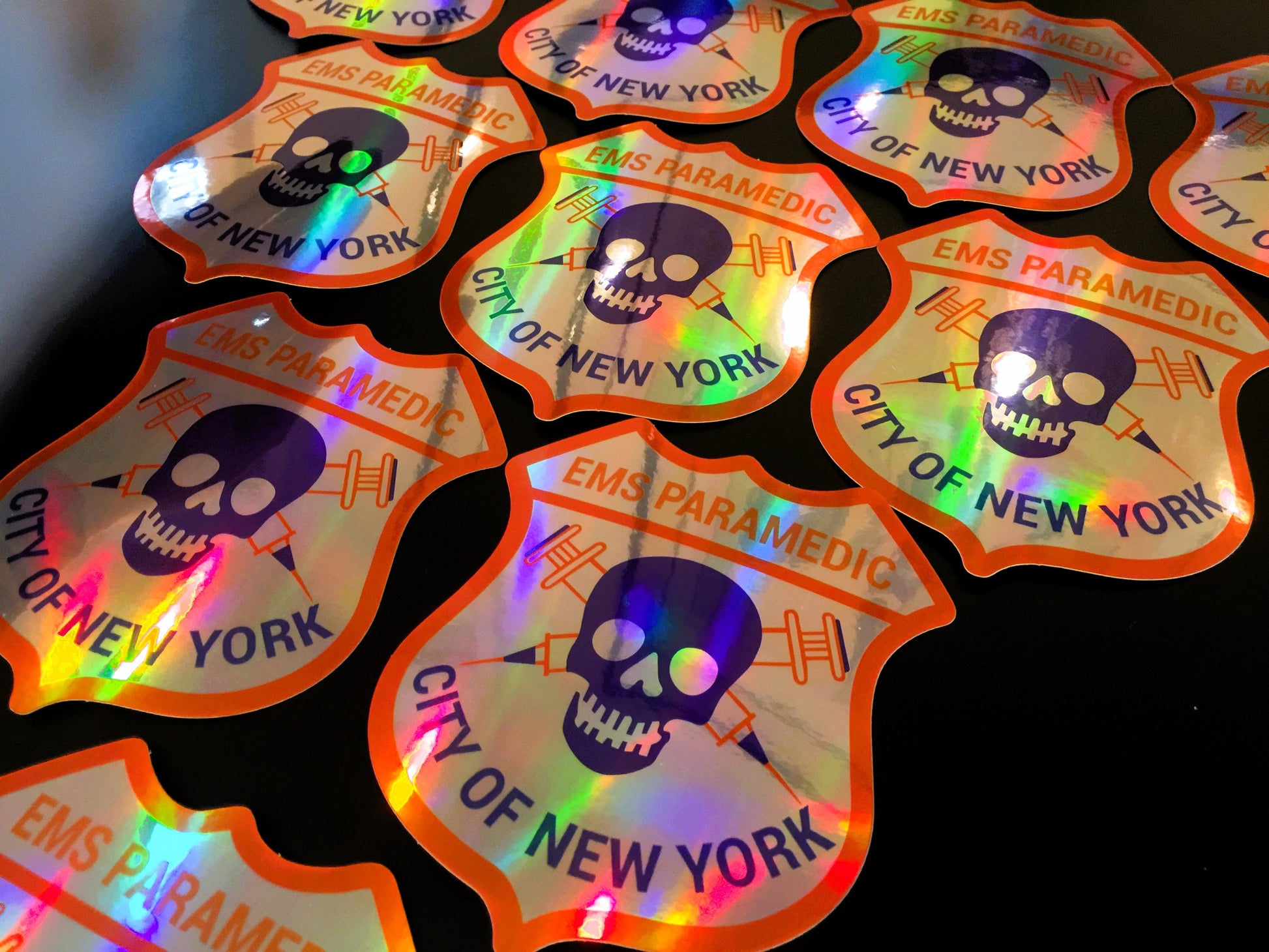 A close up view of the NYC EMS Paramedic Patch holographic stickers from Skell City against a black background.