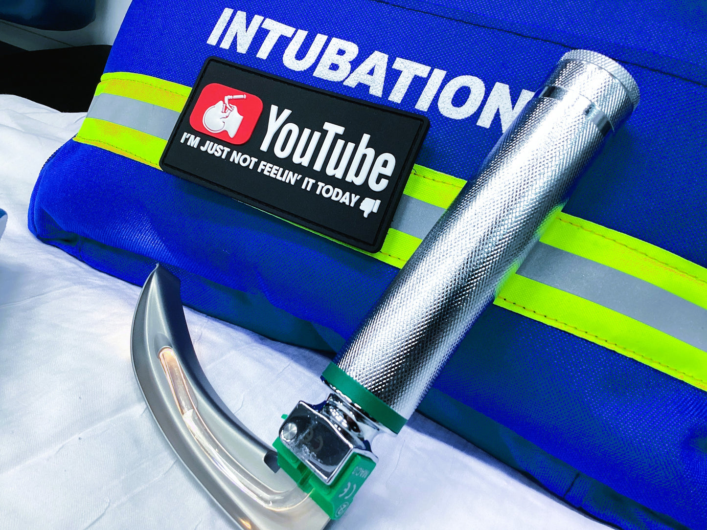 YouTube intubation PVC Velcro Patch attached to blue reflective intubation bag, next to laryngoscope blade and handle.