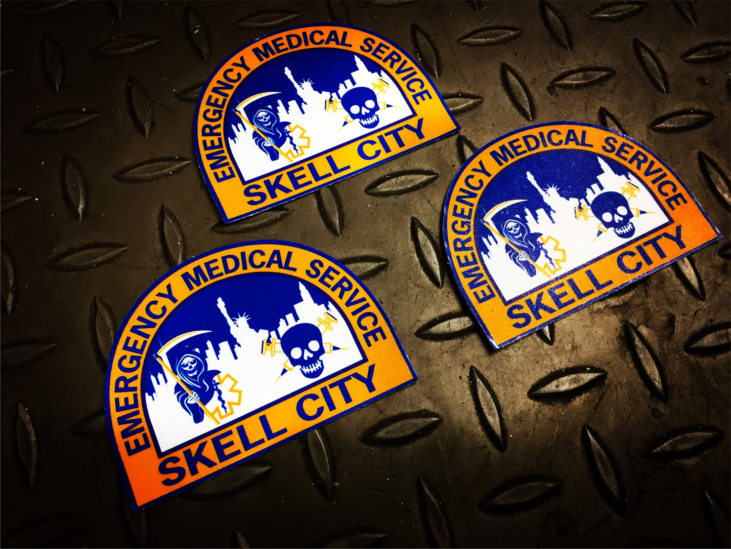 Old NYC EMS patch stickers from skell city against a dark gridiron grey background.