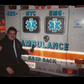 EMT Frankie the Fish smiling while holding an old brick radio pointing at the back of his NYC EMS ambulance where 'frankies bus,no skells' is written in dust