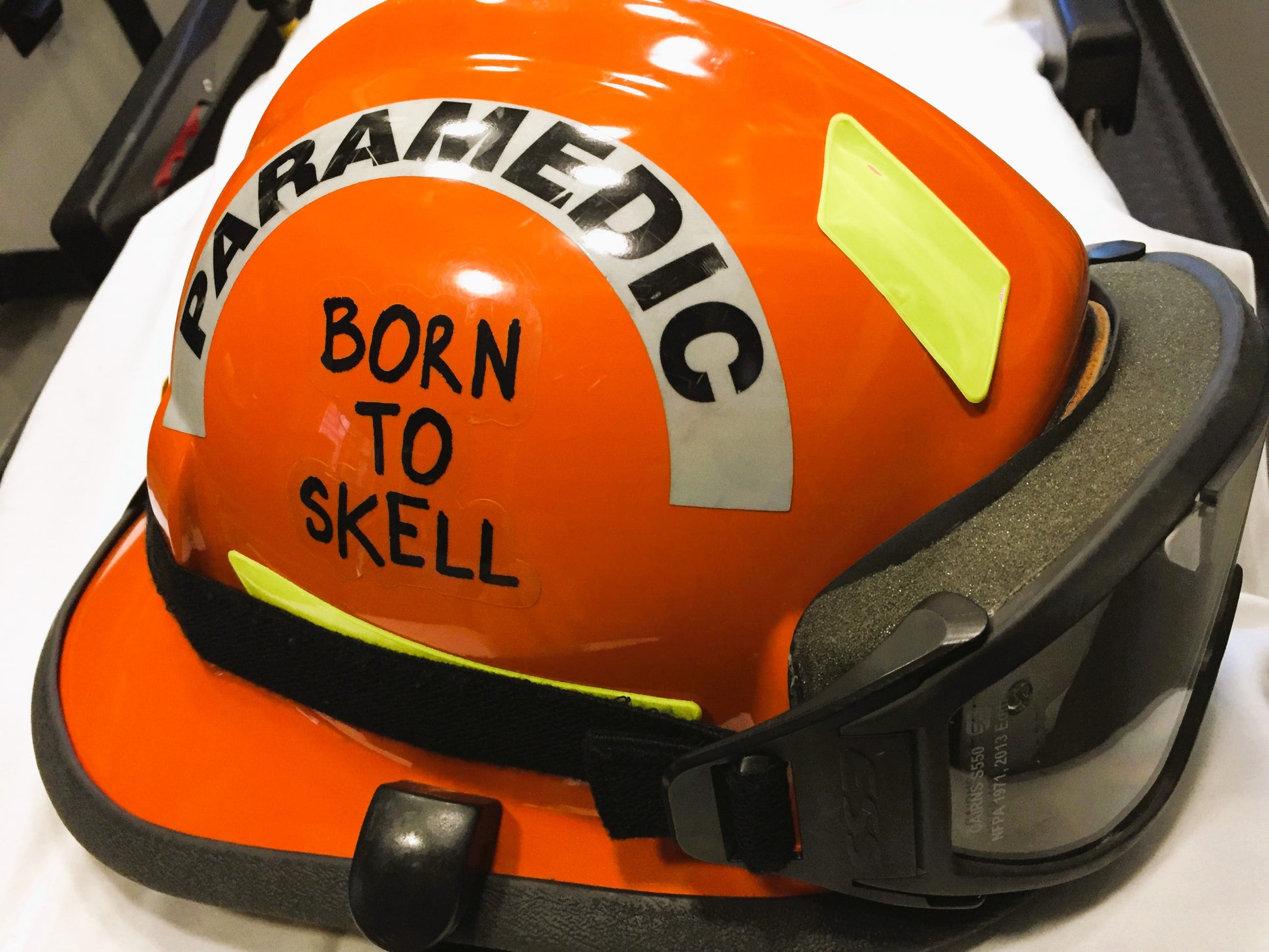 Born to Skell clear sticker from skellcity, applied to the side of an orange ems bunker gear helmet.