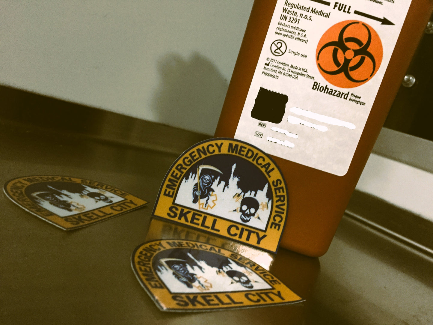 NYC EMS HHC patch reflective stickers spread out next to a covidien biohazard sharps container.