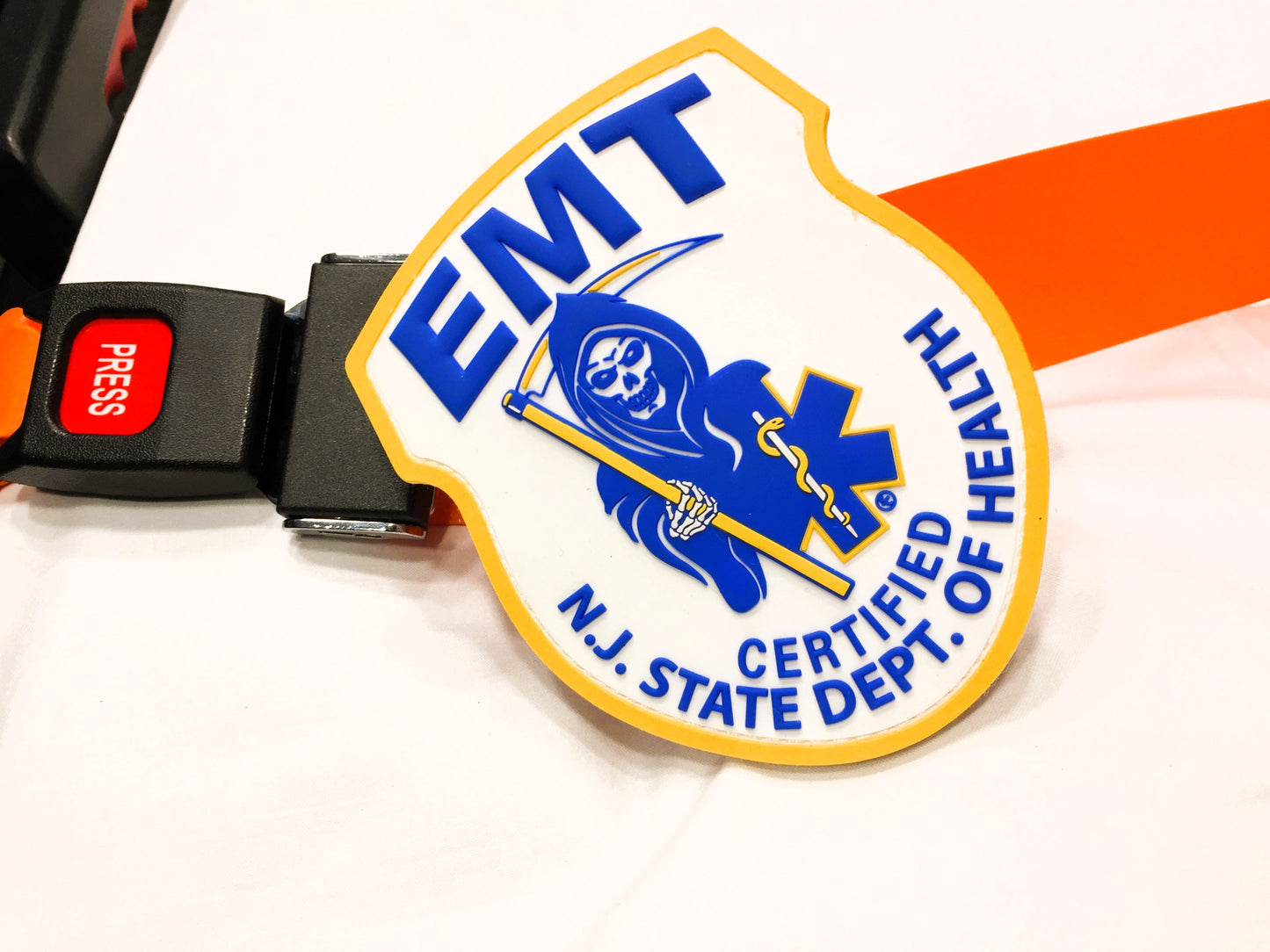 NJ EMT patch, from skell city, leaning up against orange stretcher strap buckle.