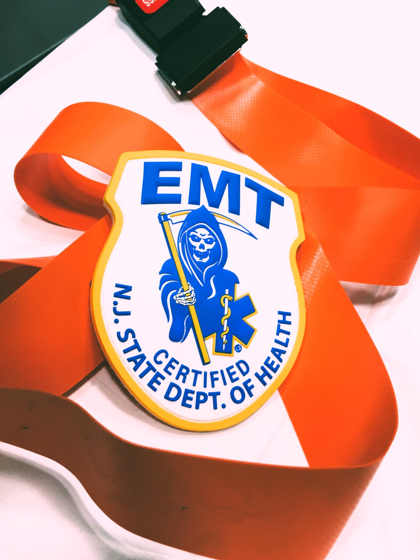 NJ EMT Patch strapped up with a bright orange stretcher strap, against a white hospital sheet background. 