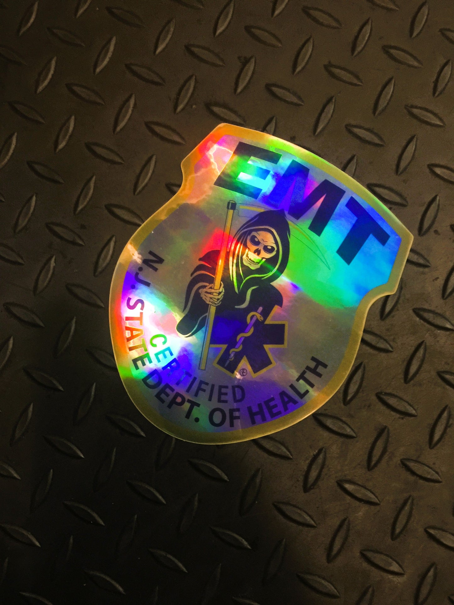 NJ EMT Patch in holographic sticker form up against a gray grid iron background.