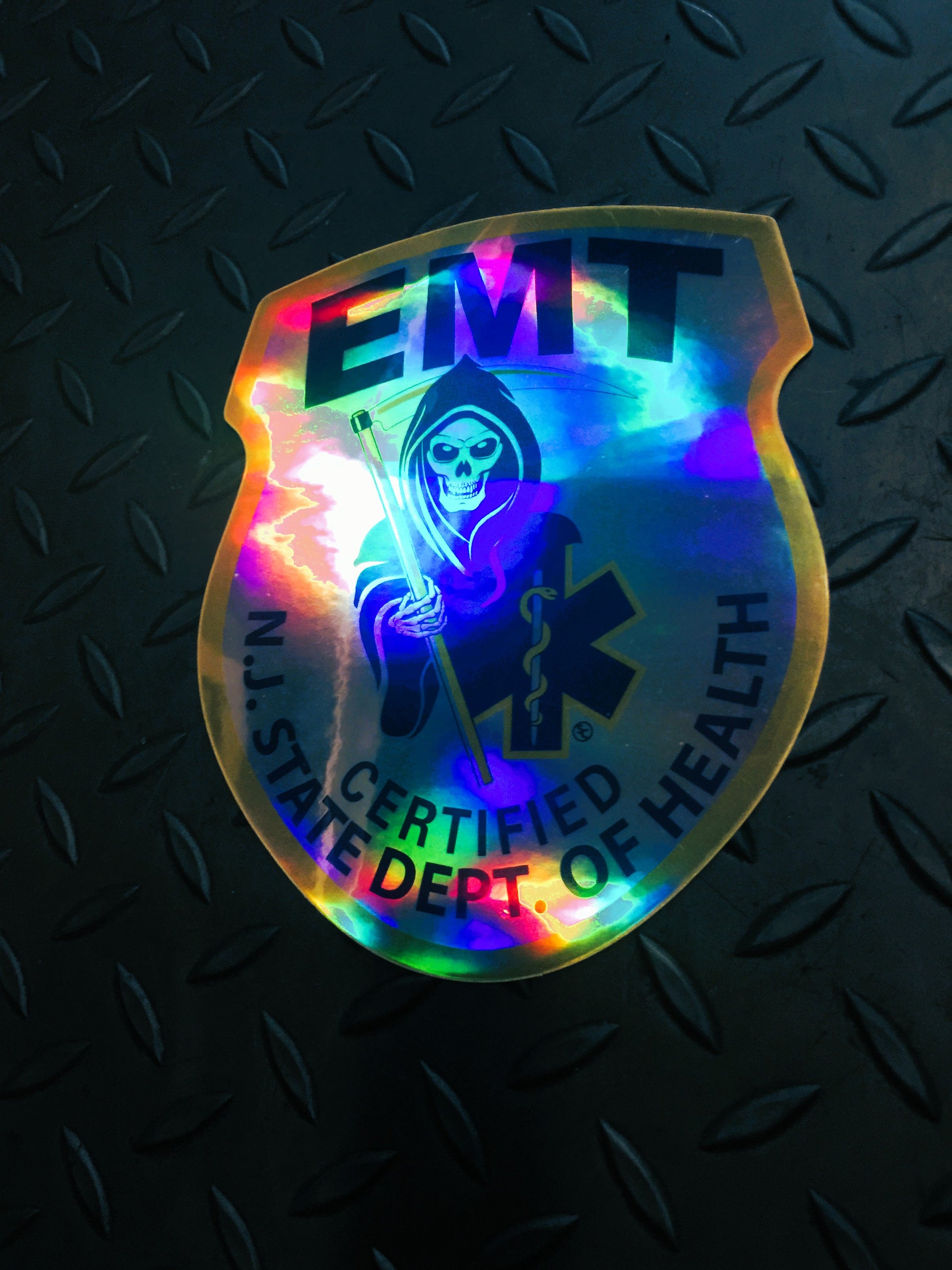 NJ EMT Patch in a holographic sticker against a dark gray gridiron background.