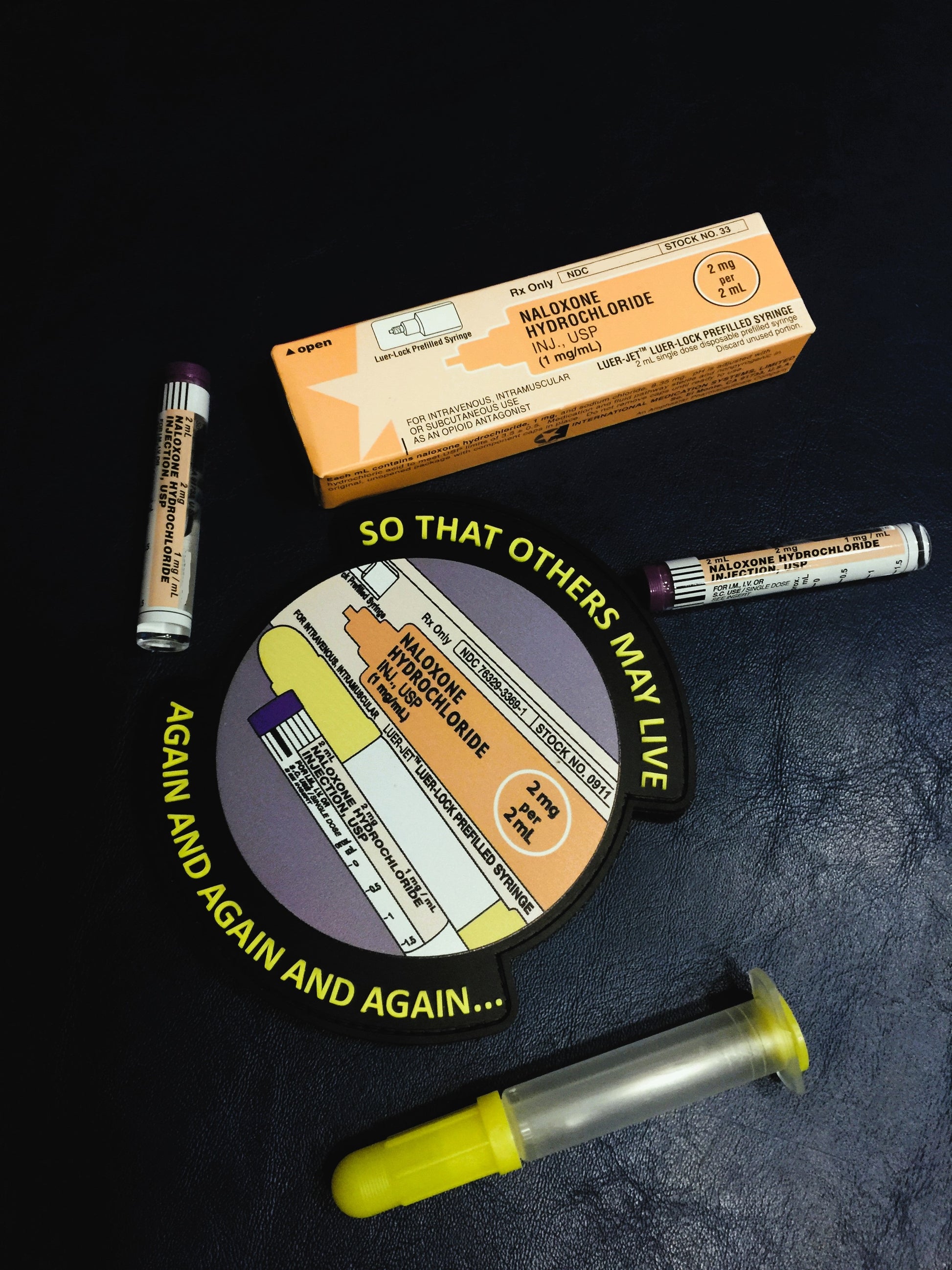 So that others may live PVC Velcro Narcan patch next to a box and vials of Naloxone hydrochloride with shooters.