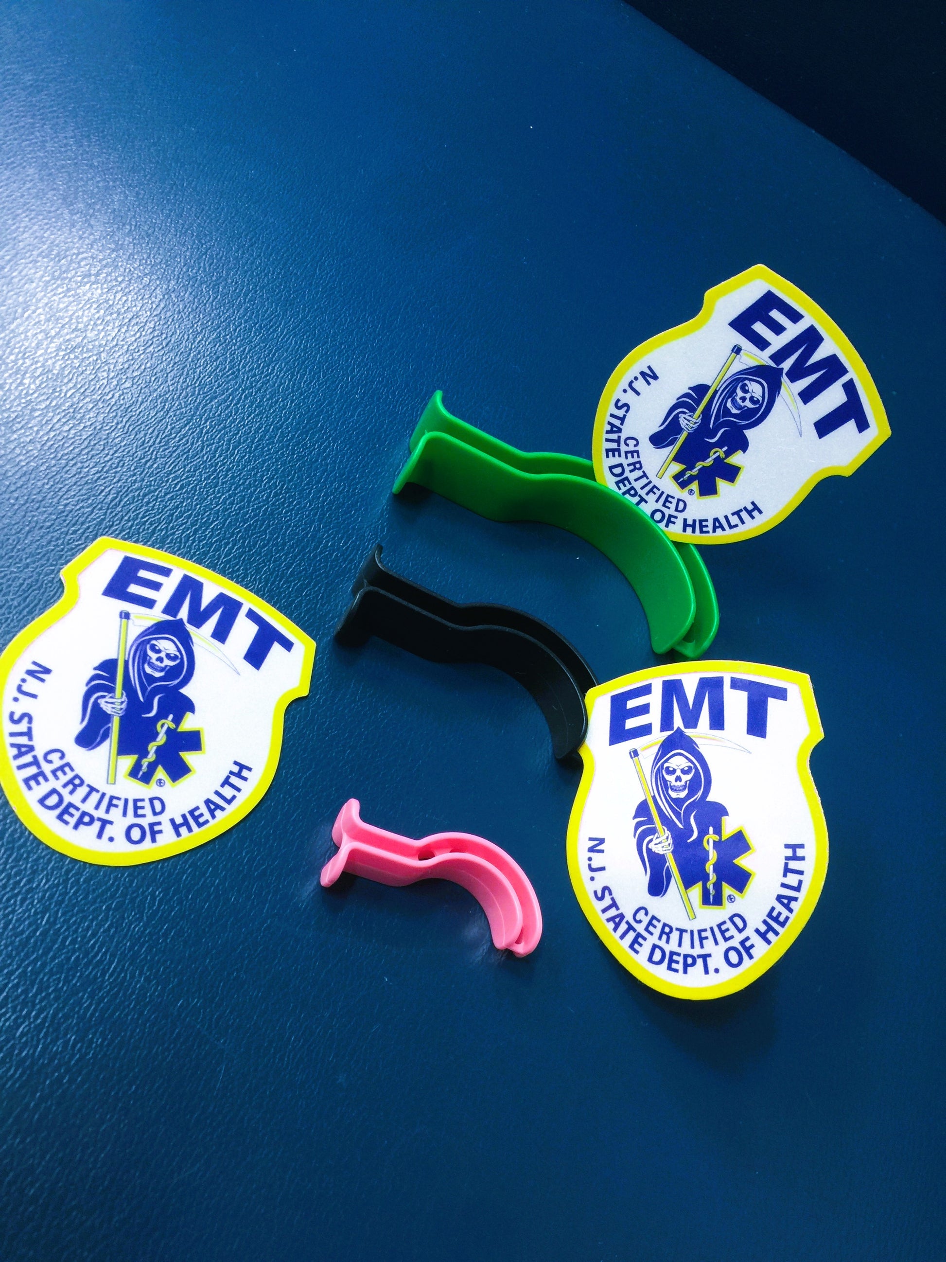 New Jersey EMT patch from skellcity Reflective Stickers hanging out with pediatric Oropharyngeal up against Blue leather bench background.