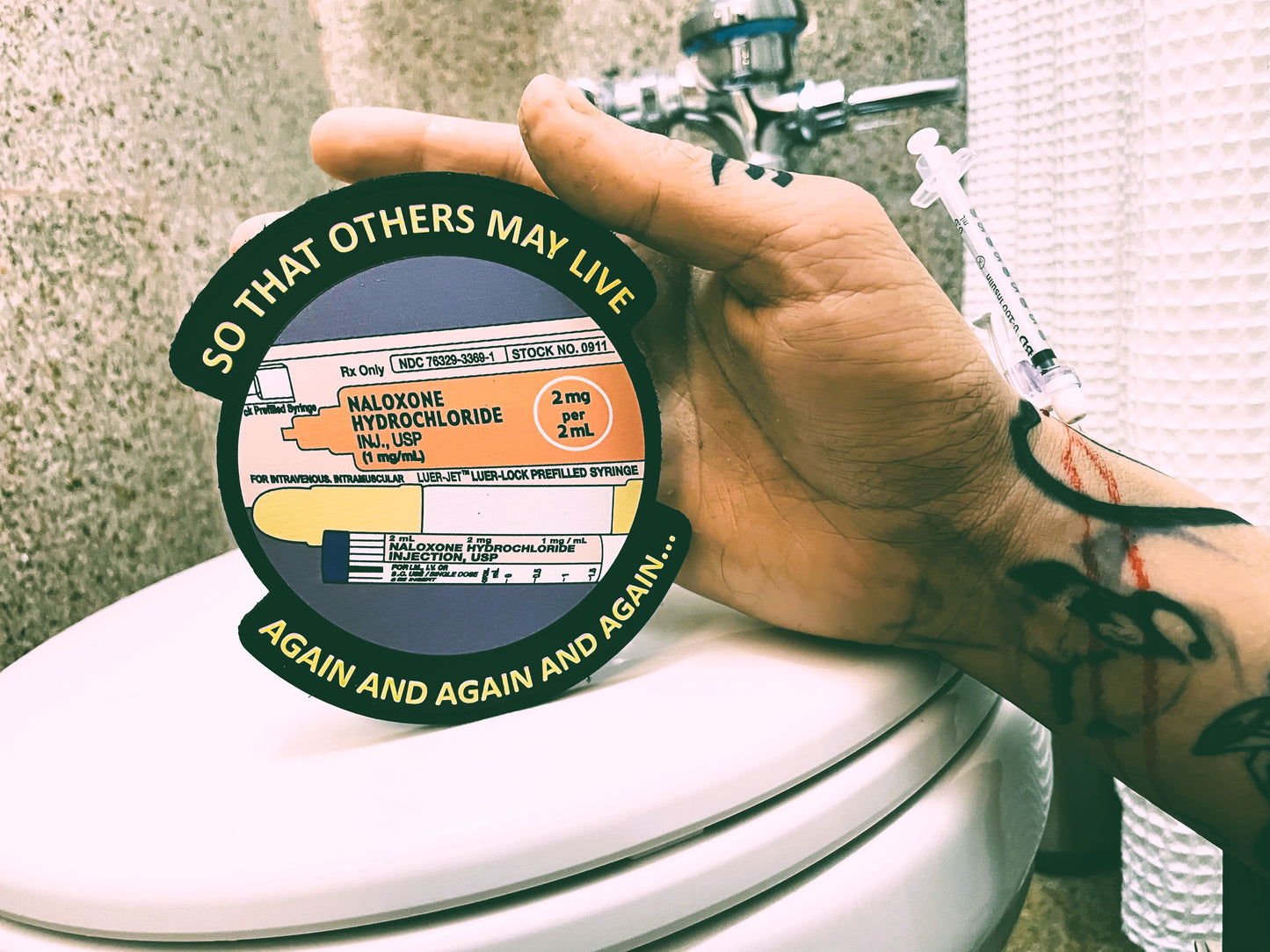 so that others may live patch being held by opioid overdose hand on top of a toilet.